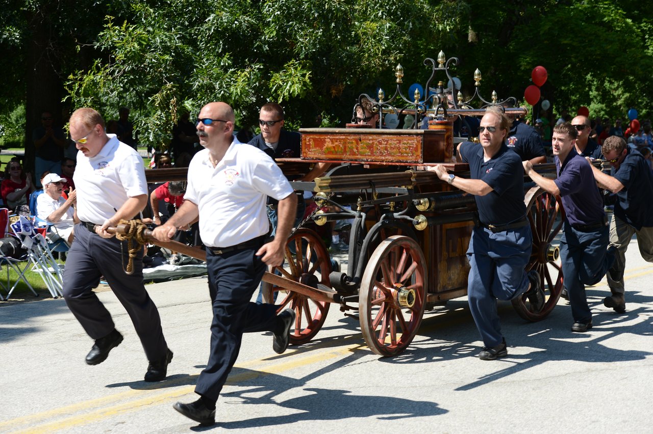 A group of people in uniform push and pull an antique fire wagon during a parade.
