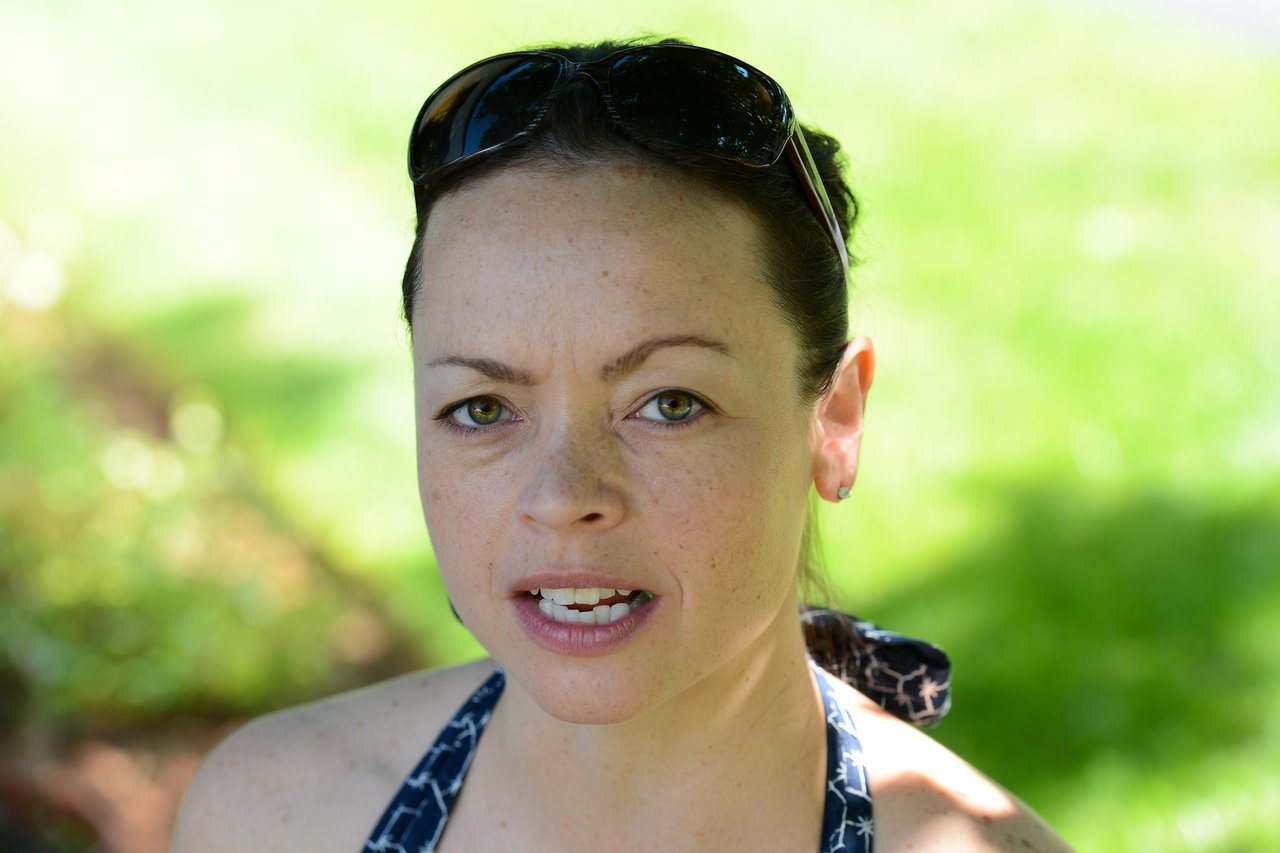 A woman with sunglasses on her head looks toward the camera, speaking during an outdoor Fourth of July parade.