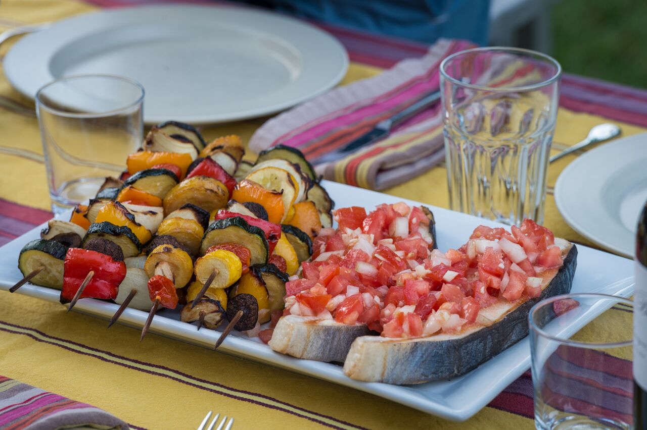 Grilled vegetable skewers and fish topped with tomatoes on a plate at an outdoor 4th of July party.