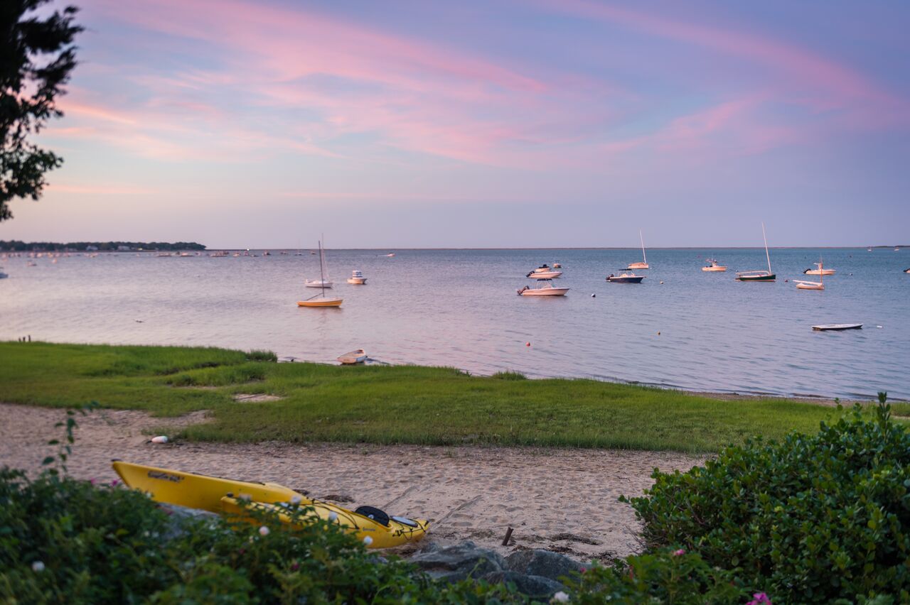 Boats anchored in calm water near a sandy beach at sunset.