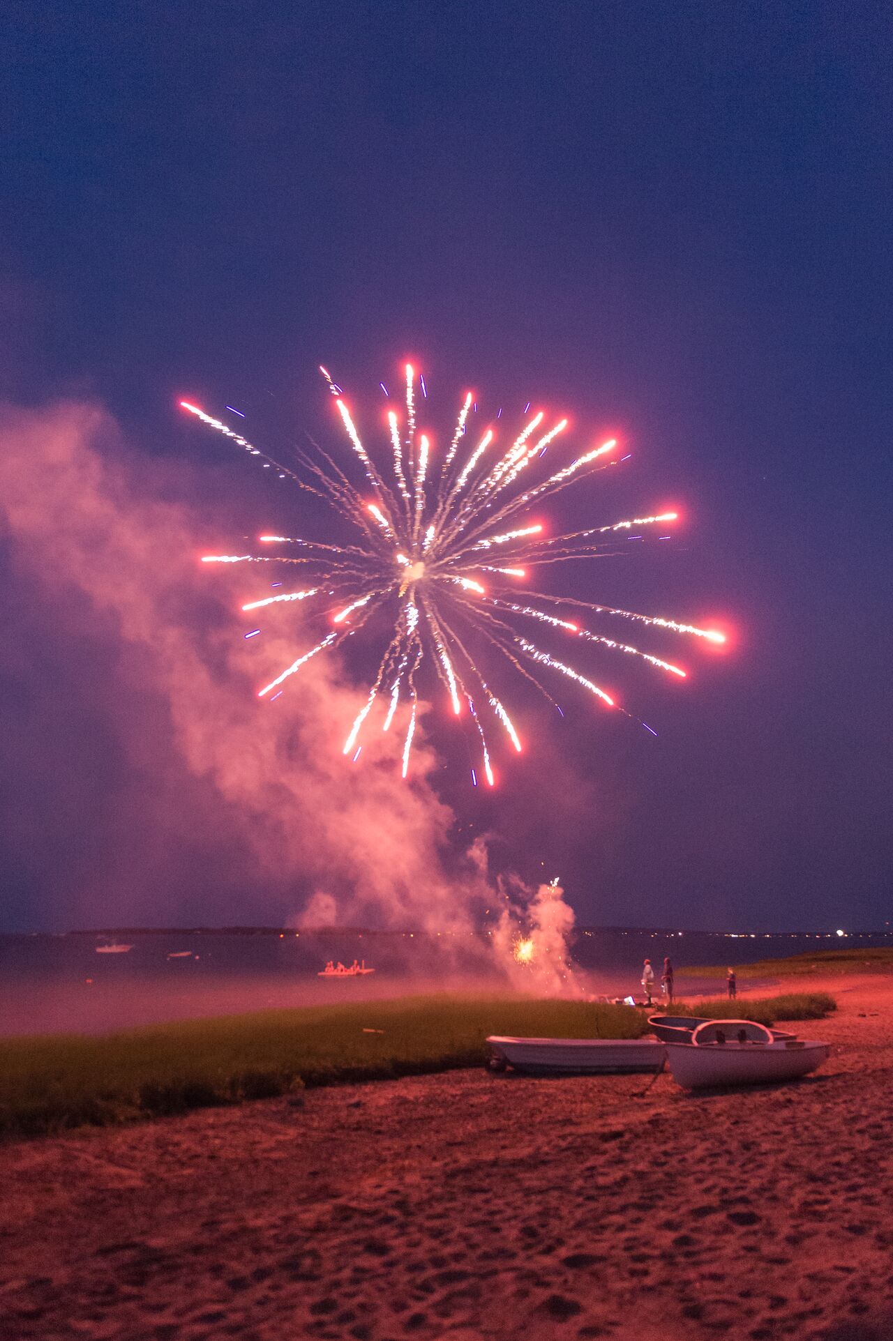 Fireworks light up the night sky on the beach as people watch during a 4th of July celebration.