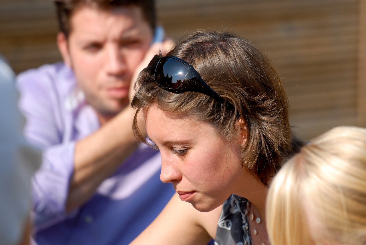 A woman with sunglasses on her head looks down, while a man in a purple shirt sits behind her.