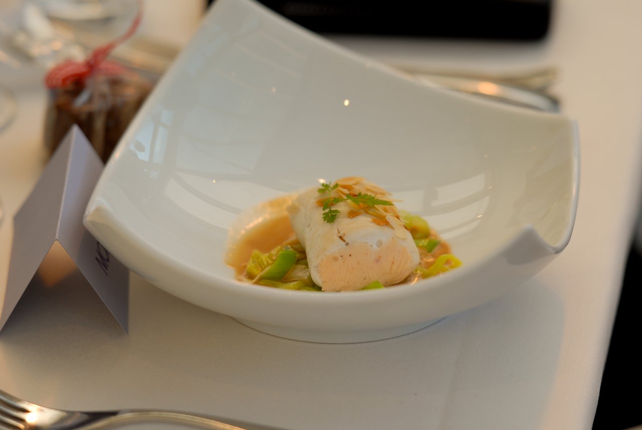 A plated dish with a salmon mousse, garnished with herbs and almonds, served on a white tablecloth.