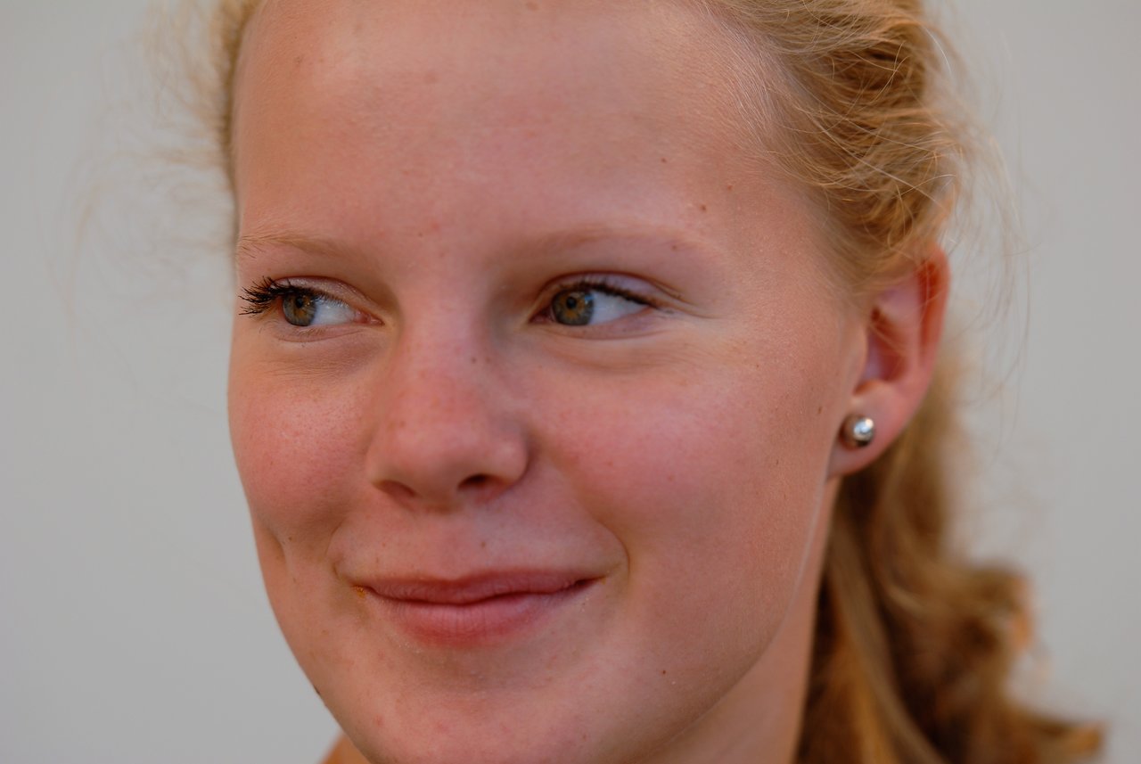 A young person with light skin and curly hair smiles softly while looking to the side.