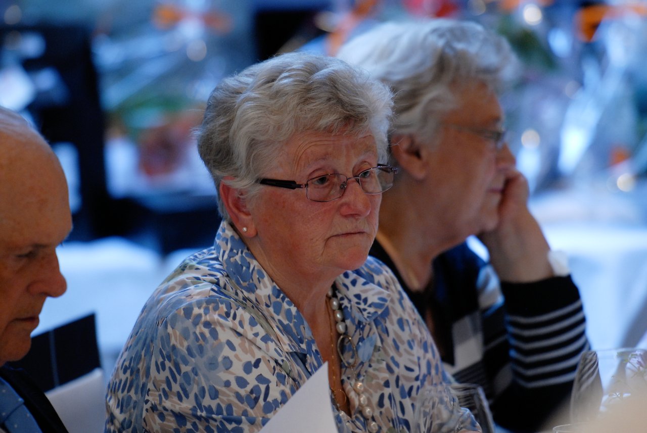 Elderly guests sit at a table, attentively listening during a 60th-anniversary celebration.