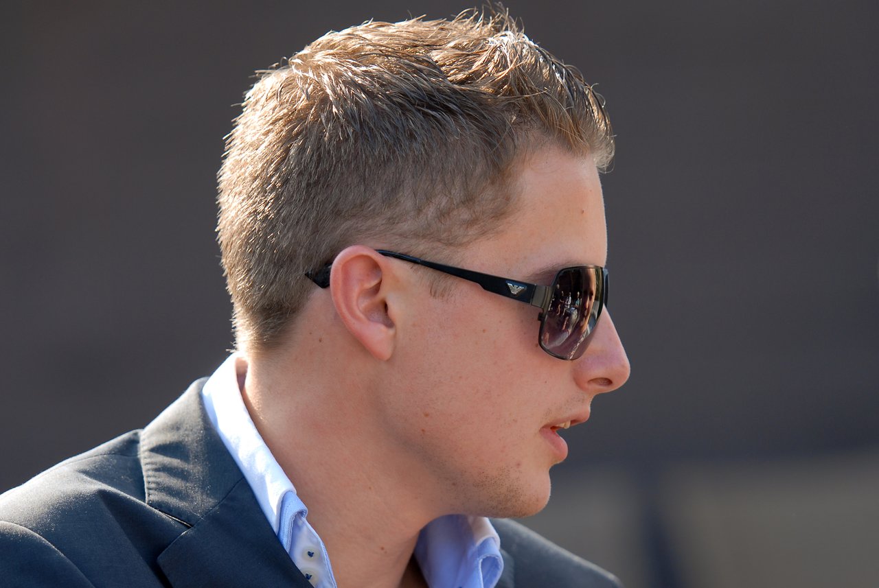 A man in sunglasses and a suit looks to the side at an outdoor gathering.