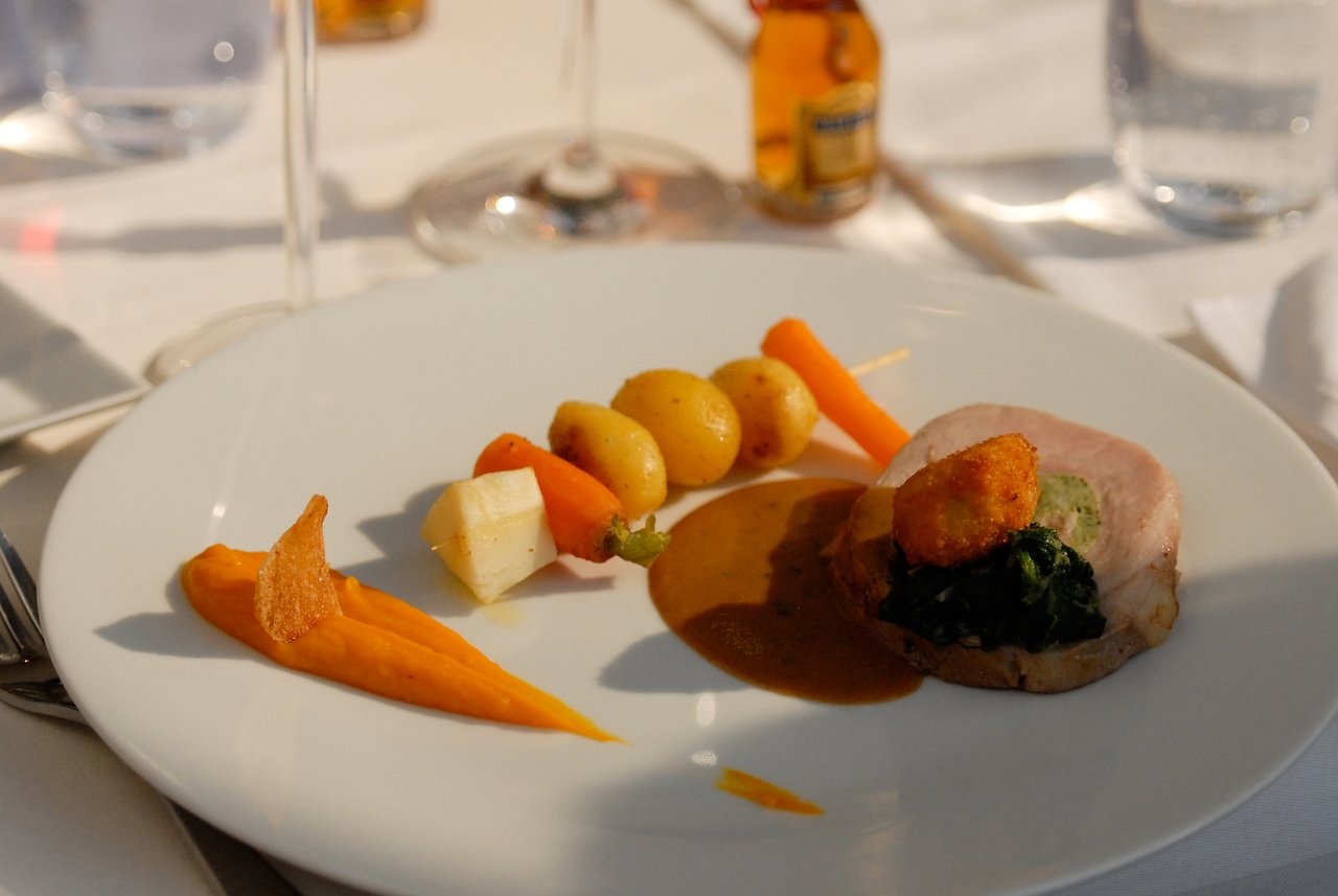 A plated meal with meat, vegetables, and sauce on a white tablecloth at a celebration dinner.