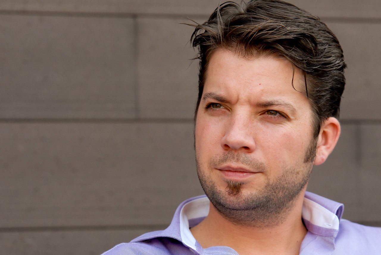 A man in a light purple shirt looks off to the side with a neutral expression.