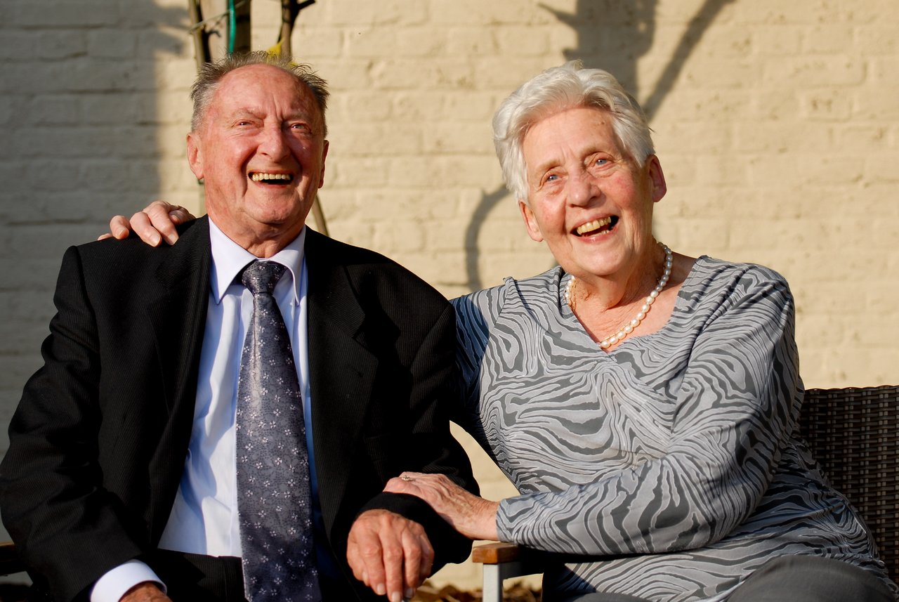 An elderly couple sits together, smiling and laughing at a celebration.