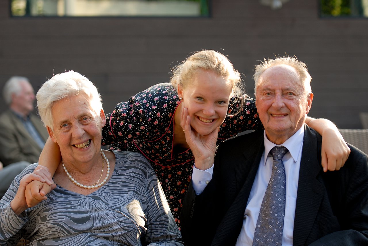 A smiling young woman embraces an elderly couple at a celebration, with all three looking happy.