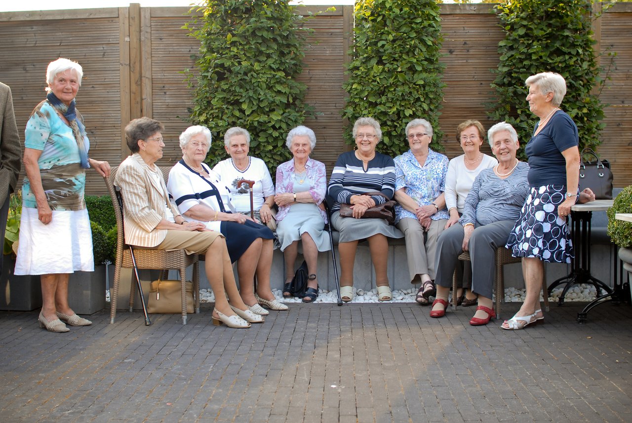 A group of elderly women sits together outdoors, smiling and chatting during a 60th-anniversary celebration.