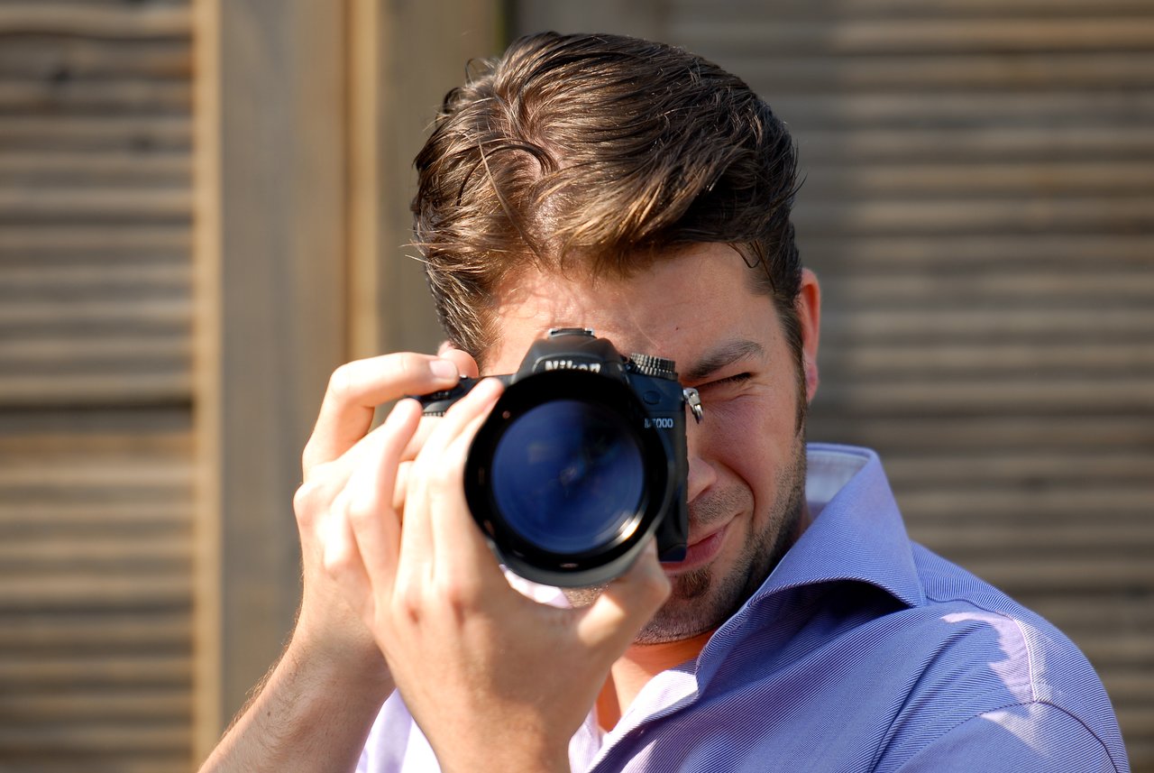 A man in a purple shirt is holding a camera and taking a photo.