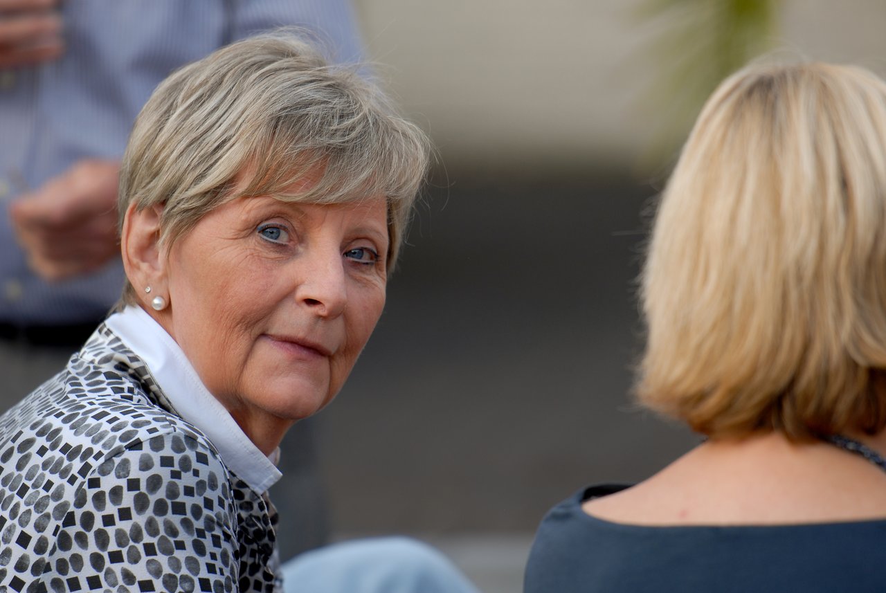 A woman with short hair looks back at the camera while sitting next to another person at a party.