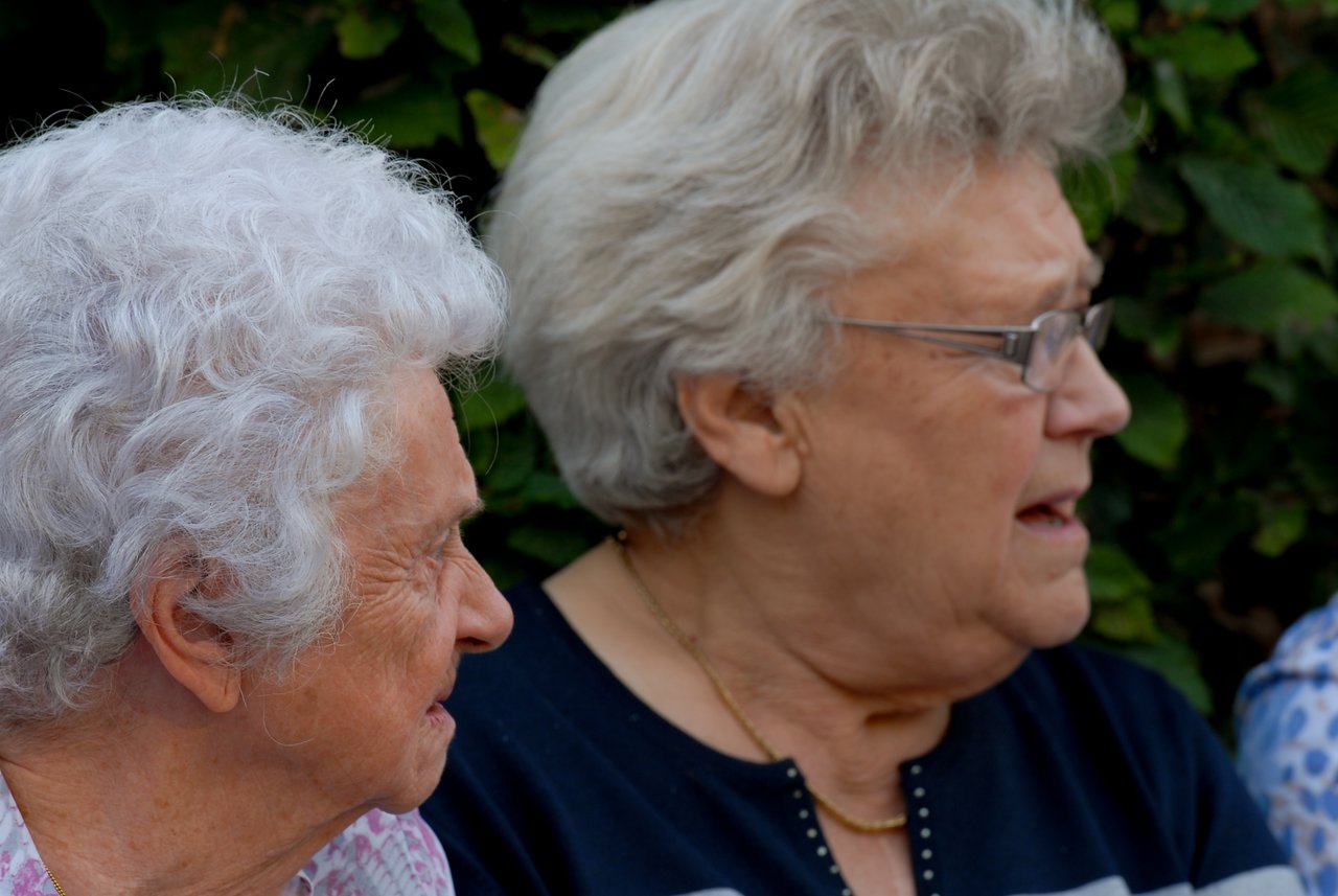 Two elderly women sitting together, engaged in conversation at an outdoor gathering.
