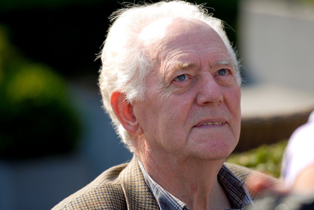 An elderly man with white hair looks up while attending an outdoor gathering.