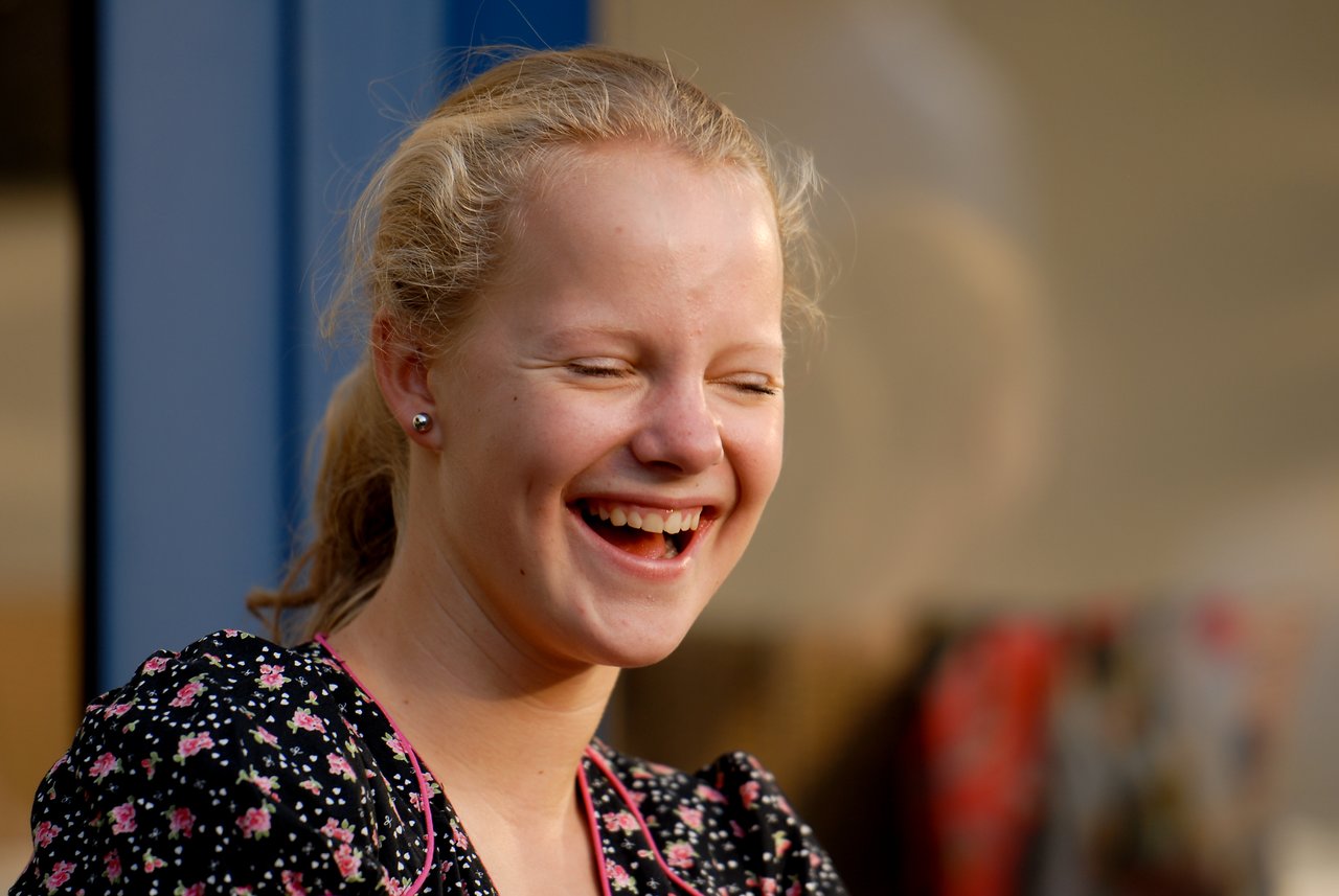 A young woman laughs with her eyes closed at a party, wearing a black floral dress.