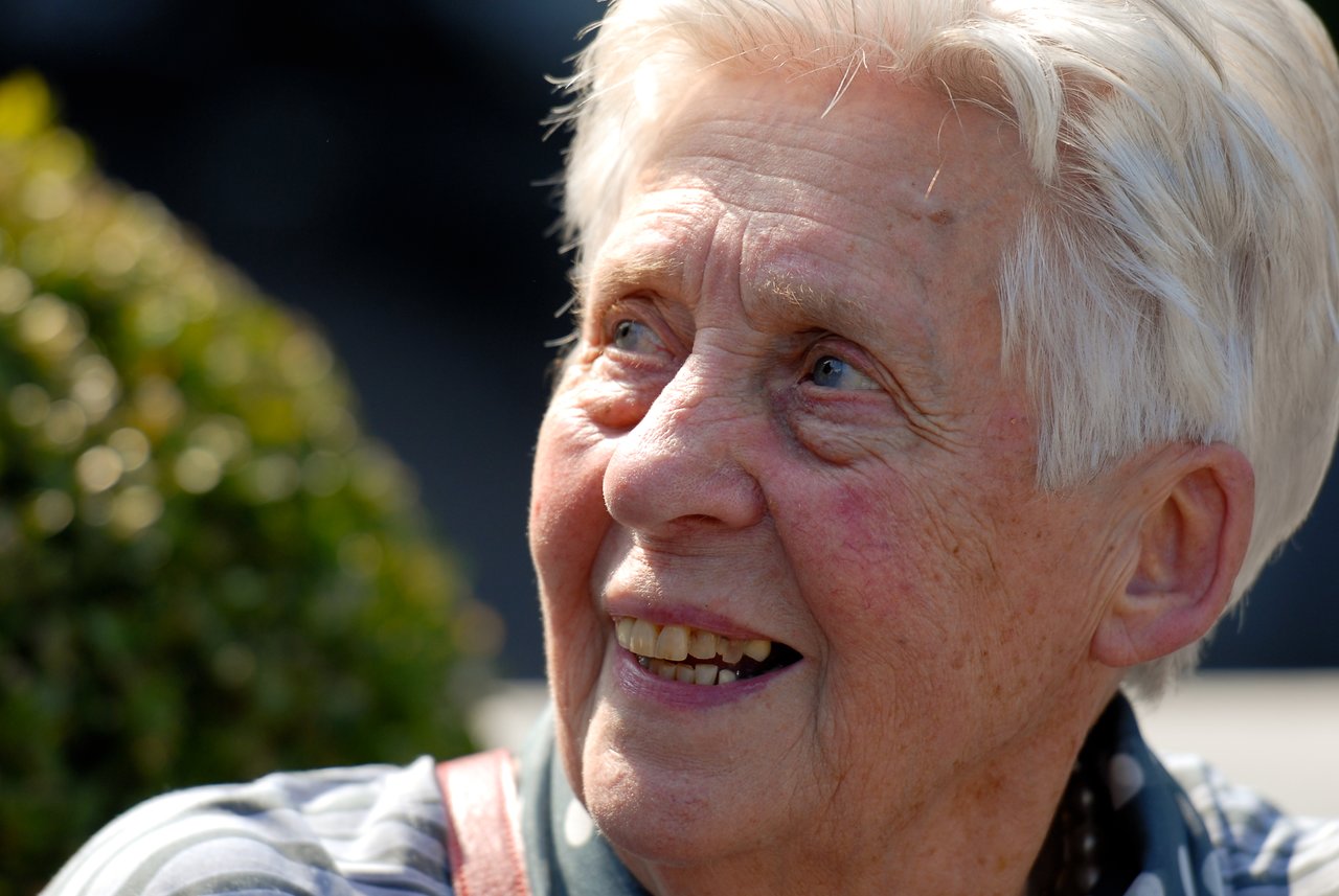 An elderly person with short white hair smiles while looking up at something during a celebration.