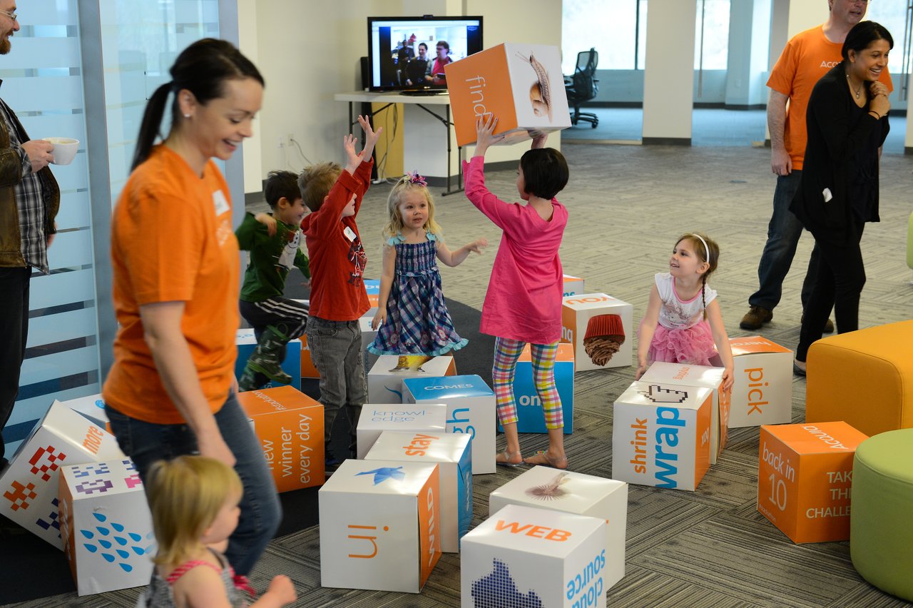 Children play with large colorful blocks while adults supervise and interact during a workplace event.