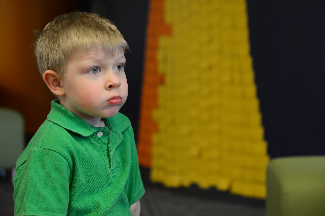 A young child in a green shirt looks off to the side with a neutral expression.