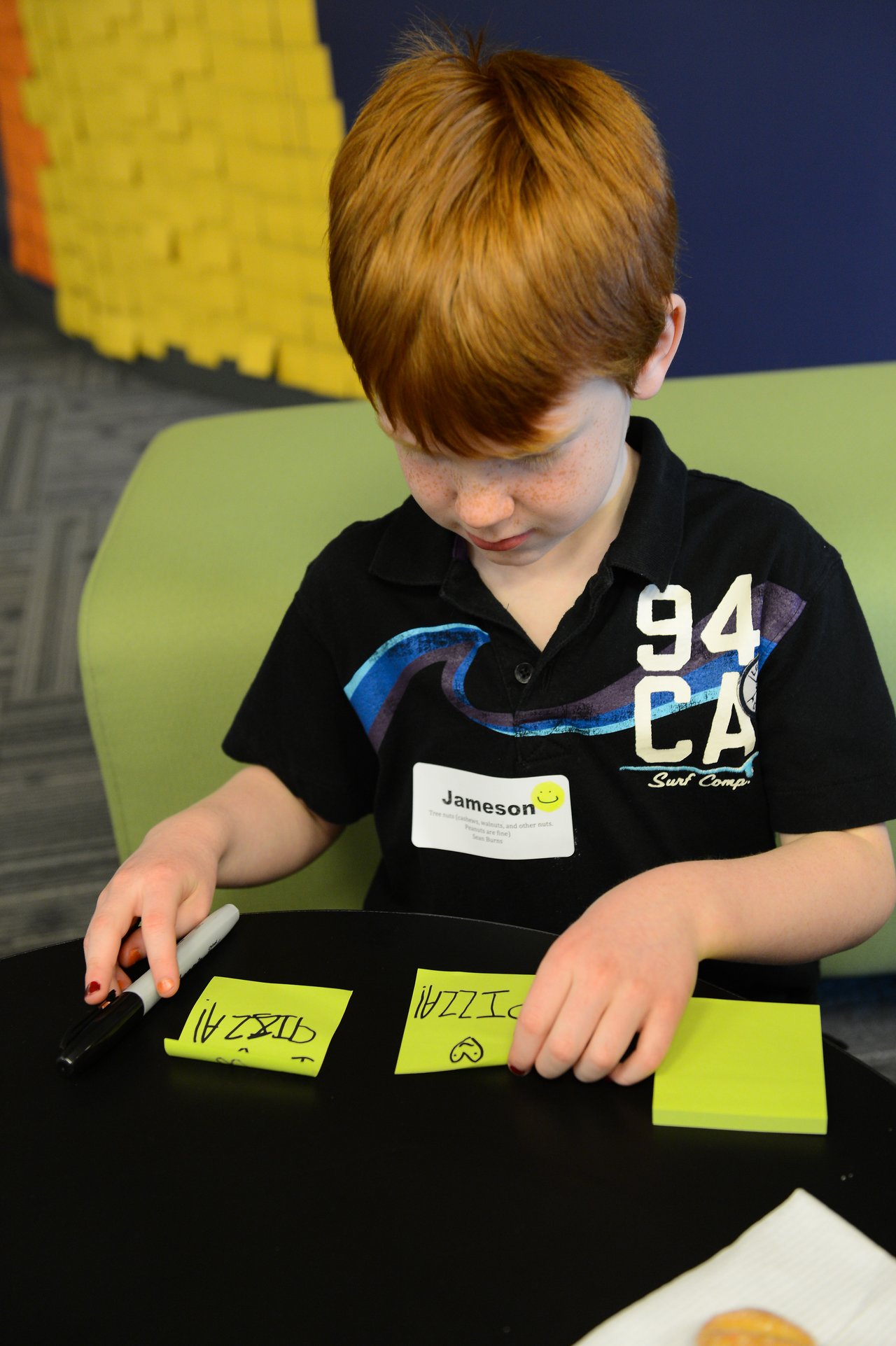 A child writes on sticky notes with a marker while sitting at a table.