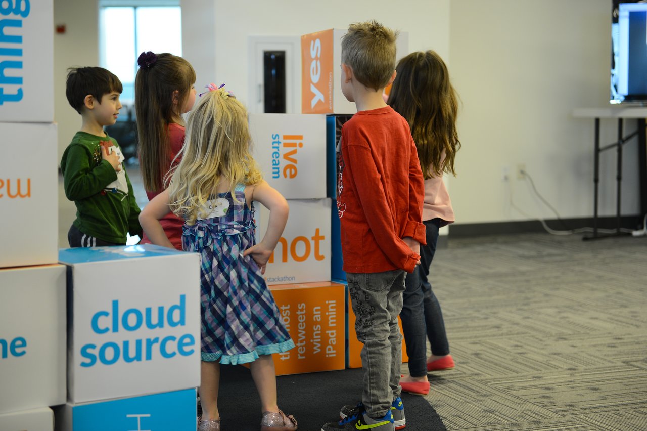 A group of children stands near large stacked blocks, looking at them during a workplace event.