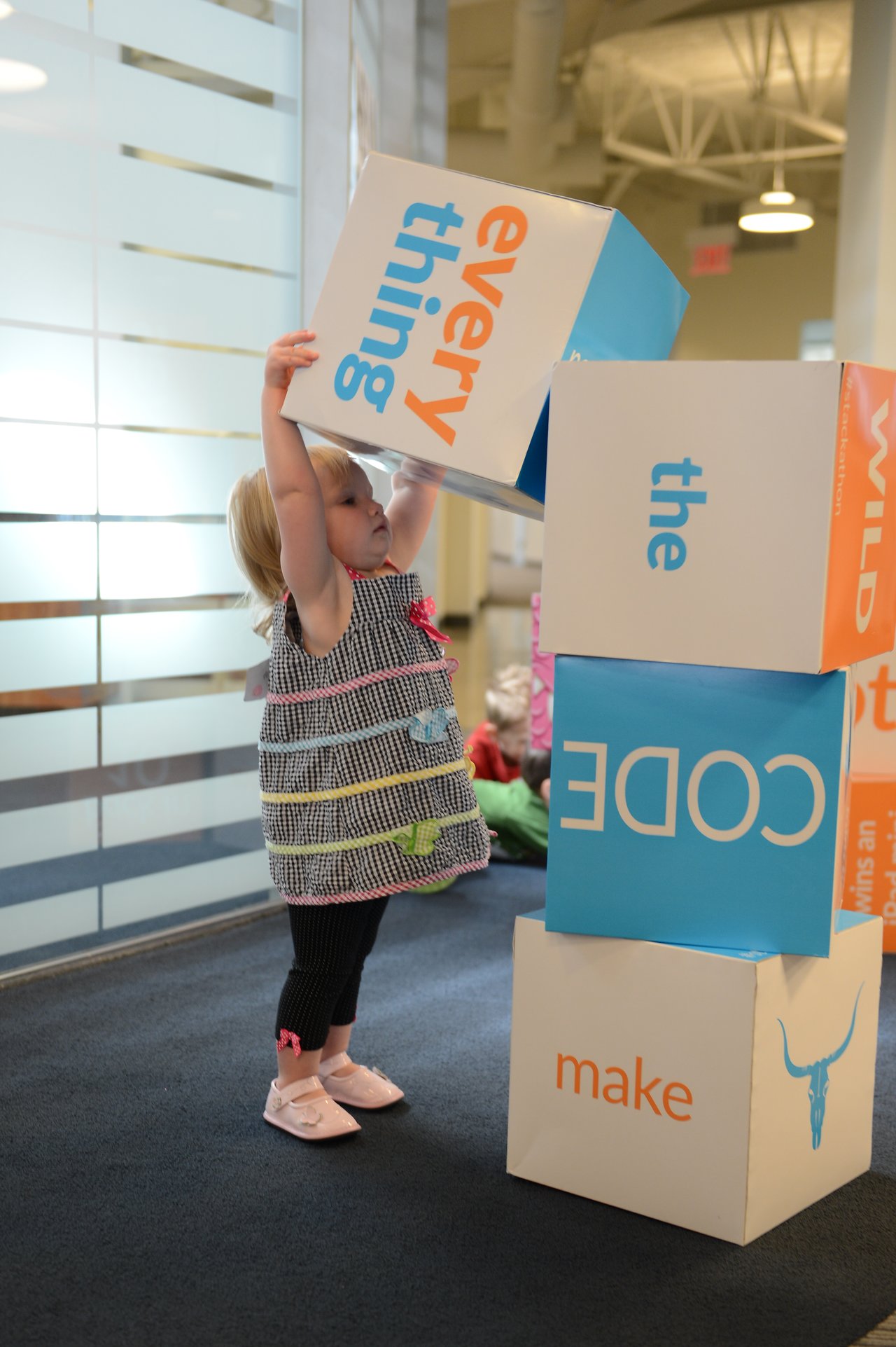 A young child stacks large colorful blocks with words in an office setting.