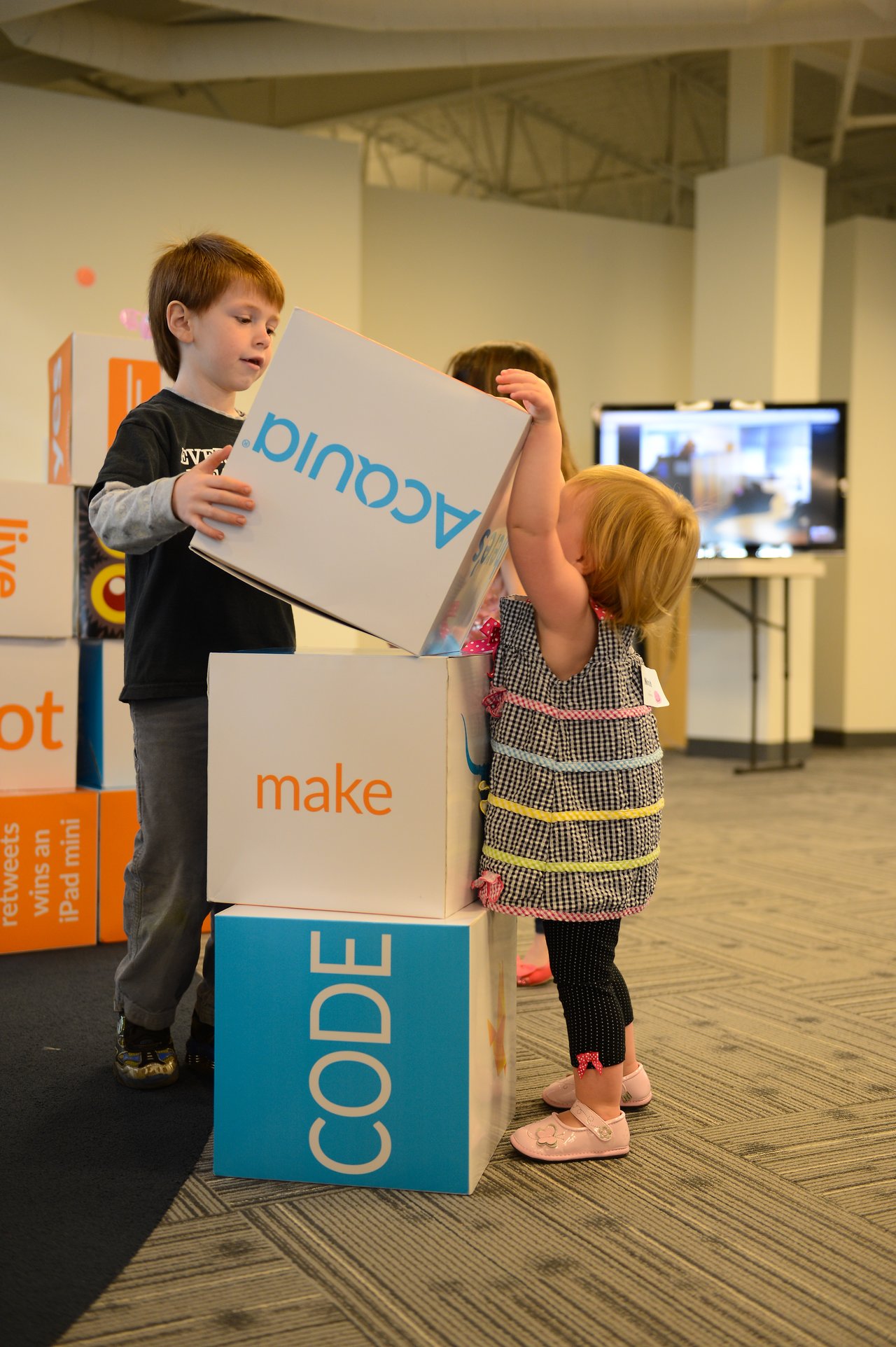 A young boy and girl stack large Acquia-branded blocks together in an indoor workspace.