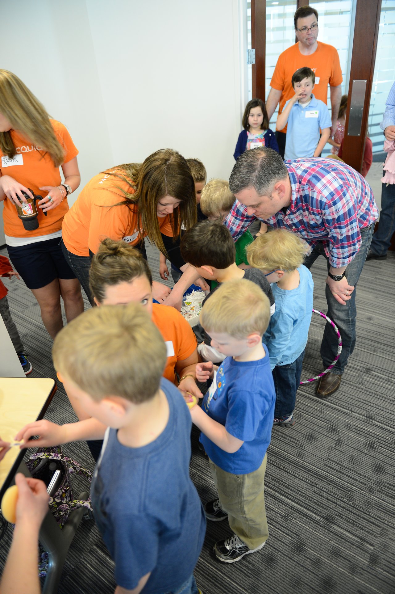 Children and adults gather around a table, engaging in an activity during a "Bring Your Kids to Work" event.