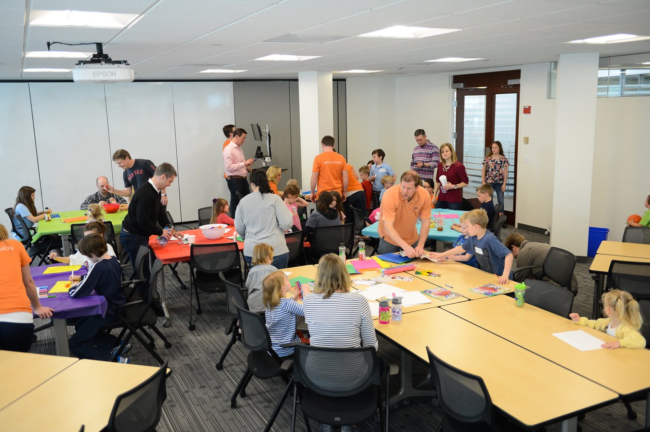 Adults and children gather in a conference room, participating in arts and crafts activities during a workplace event.