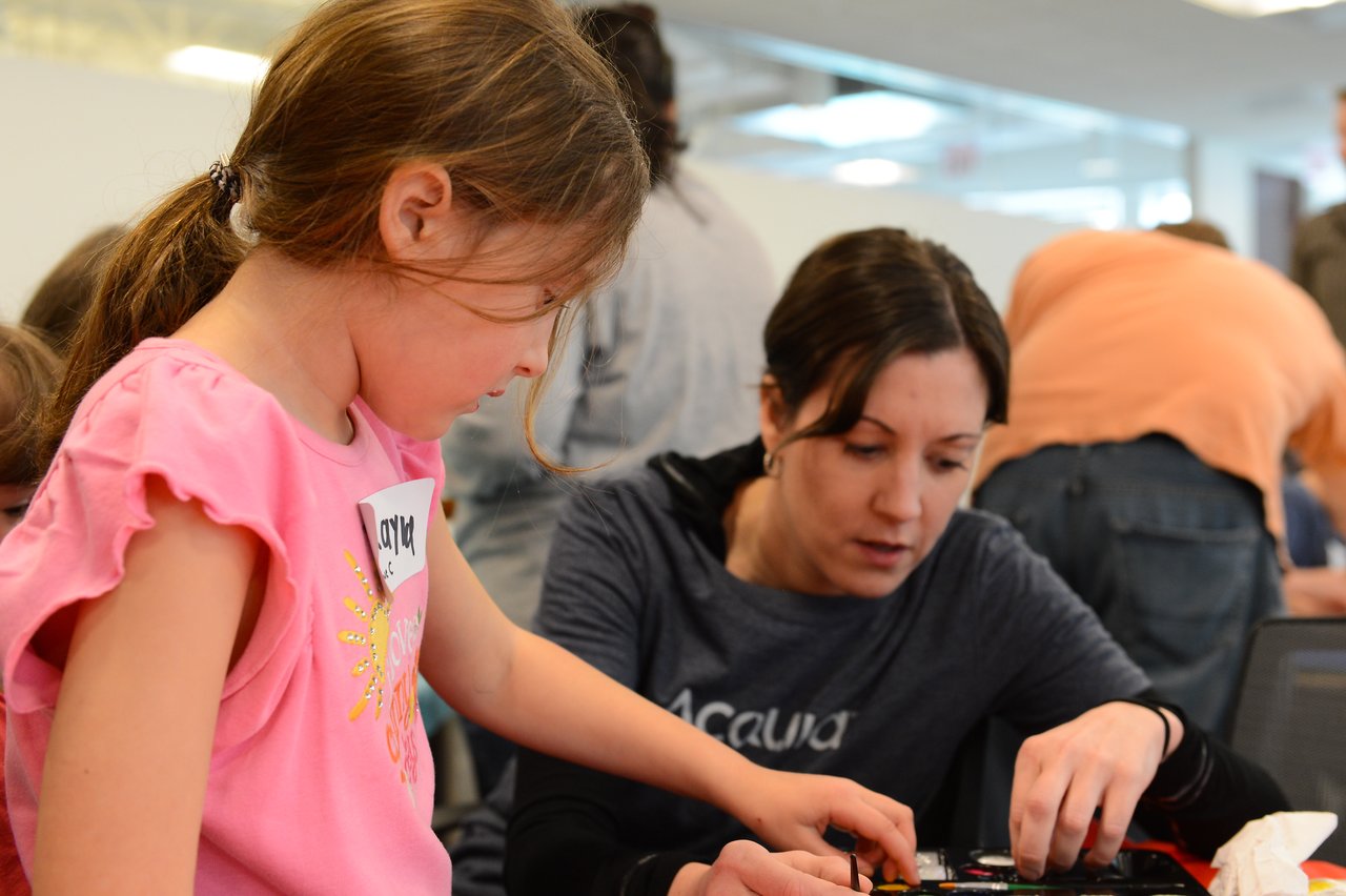 A woman and a young girl work together on a hands-on activity at a workplace event.