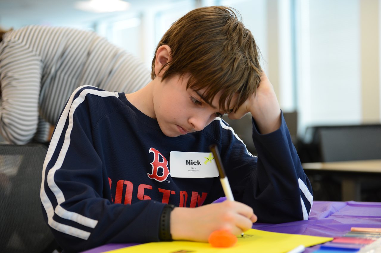 A child sits at a table, focused on drawing or writing on a colorful sheet of paper.