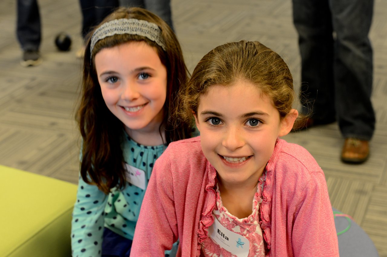 Two young girls with name tags smile at the camera during a "Bring Your Kids to Work Day" event.