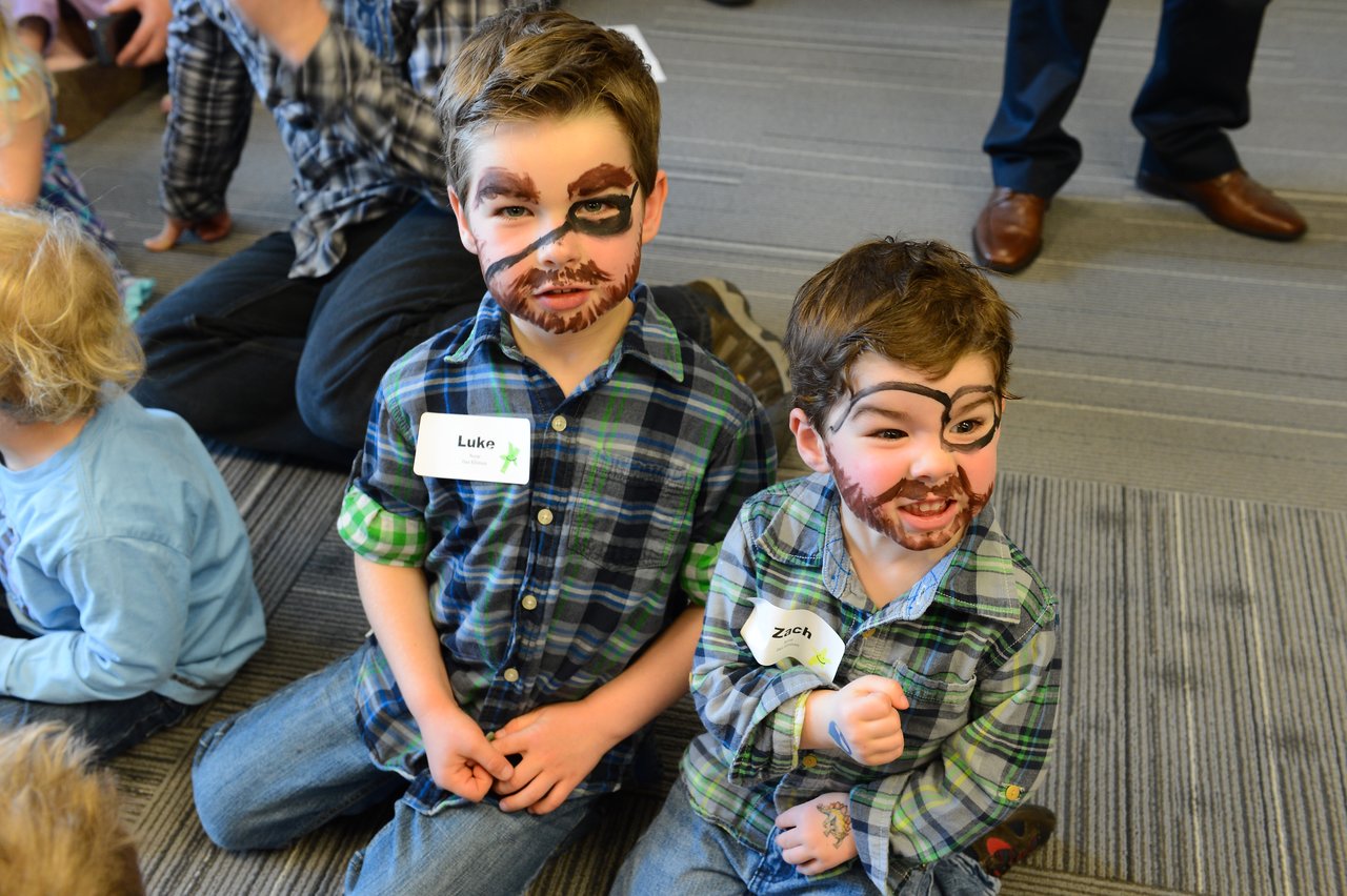 Two young children with face paint sit on the floor, smiling.