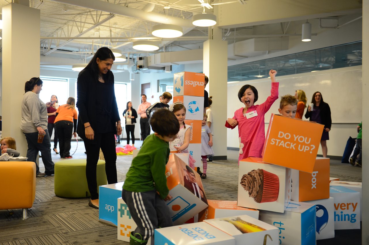 Children excitedly stack and knock over large colorful blocks while an adult watches in an office setting.