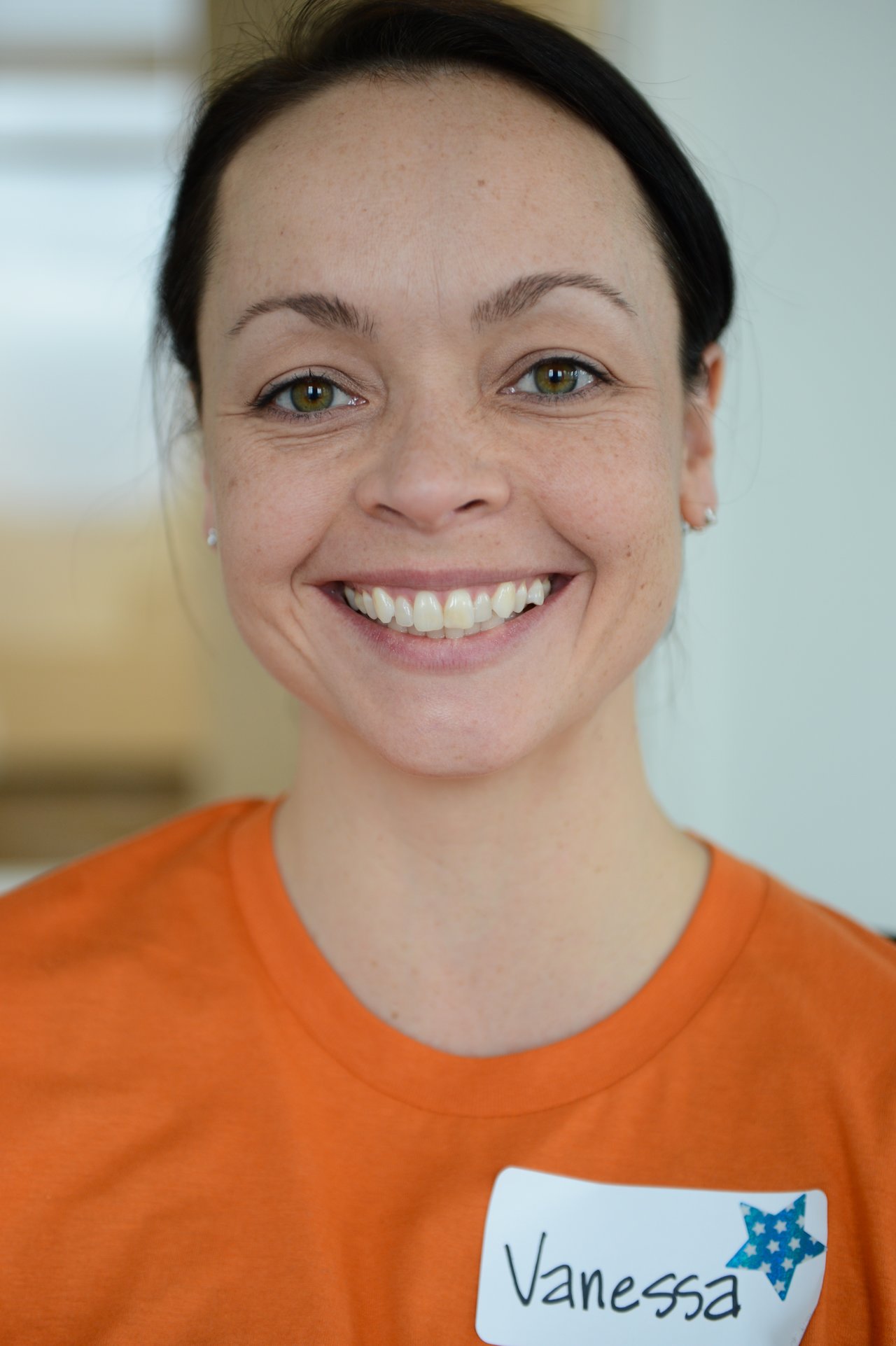 A smiling person wearing an orange shirt with a name tag that says "Vanessa.
