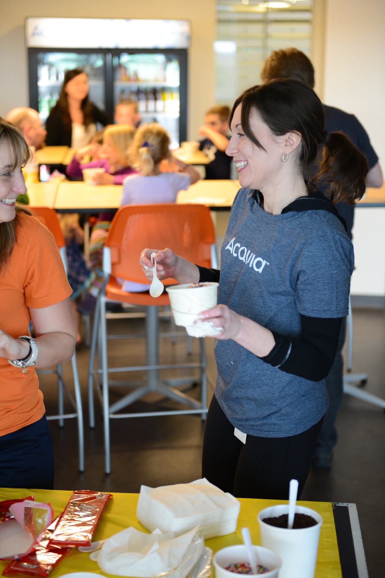 A woman in an Acquia shirt smiles while holding a cup of ice cream at a workplace event.