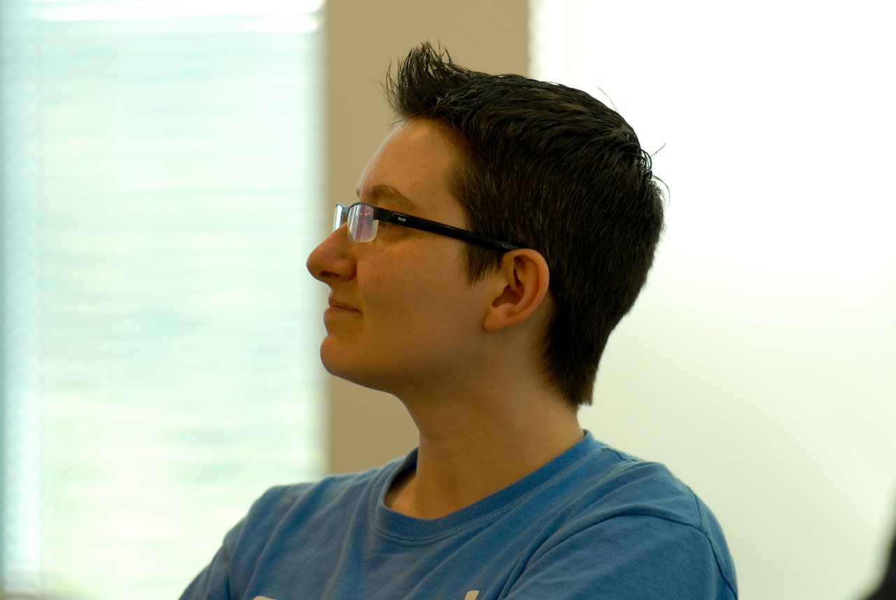 A person wearing glasses and a blue shirt listens attentively during a meeting or presentation.