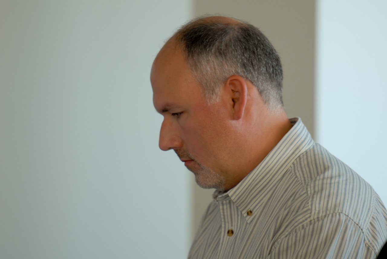 A man in a striped shirt looks down with a focused expression in an indoor setting.