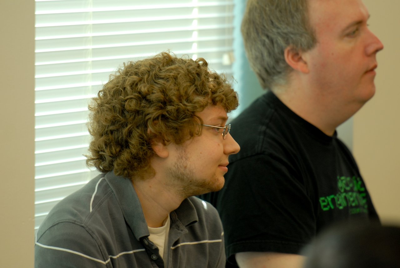 Two people sitting indoors, attentively listening to something off-camera.