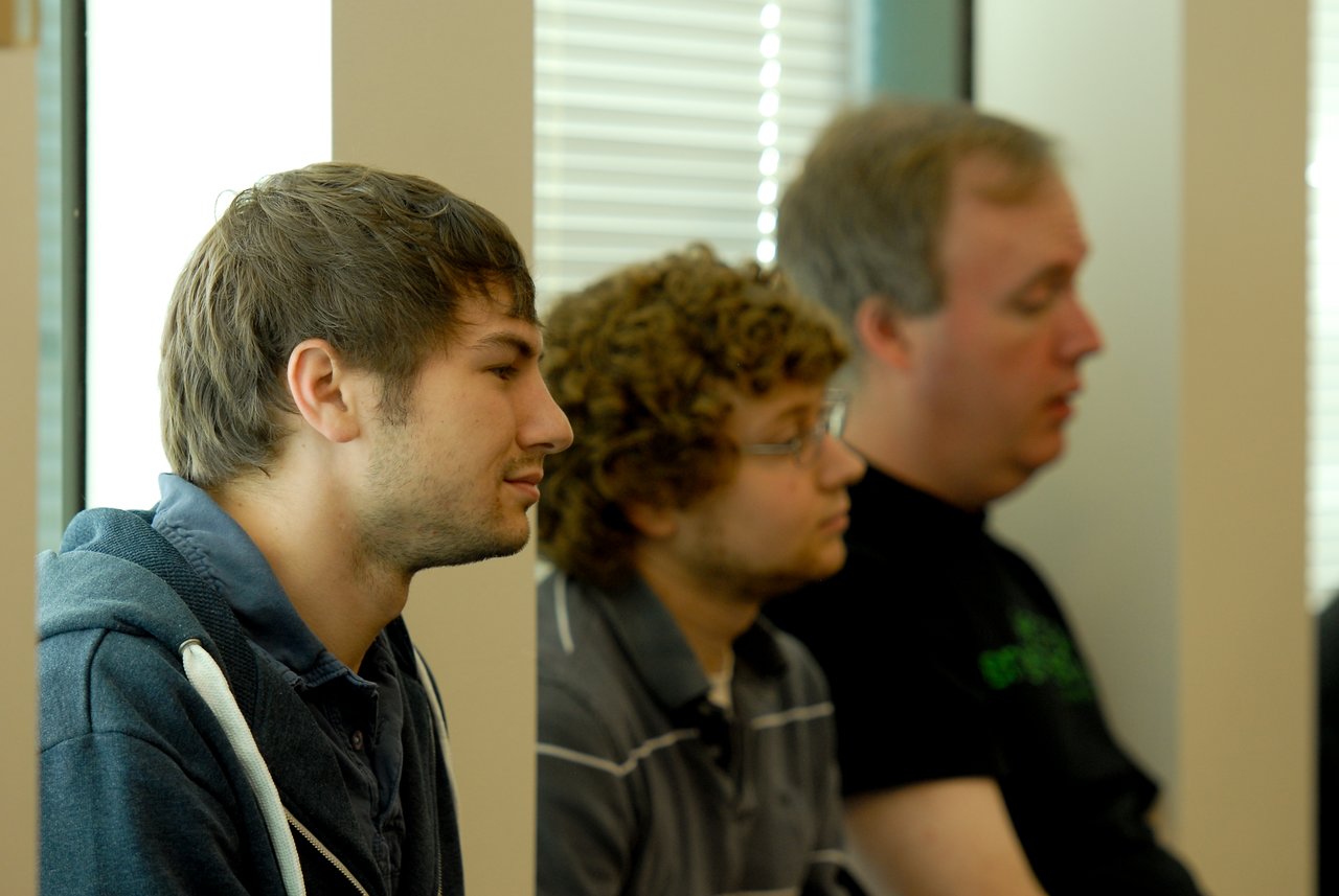 Three people sitting indoors, attentively listening to something off-camera.