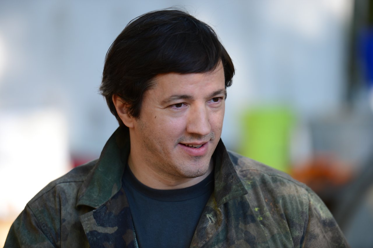 A person wearing a camouflage jacket looks to the side with a slight smile.