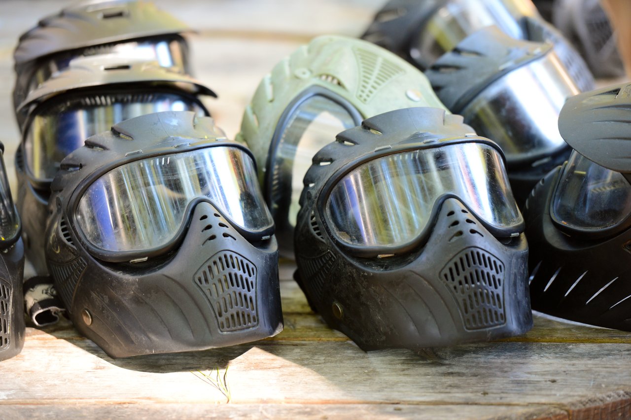 Several black and green paintball masks with reflective visors are placed on a wooden surface.