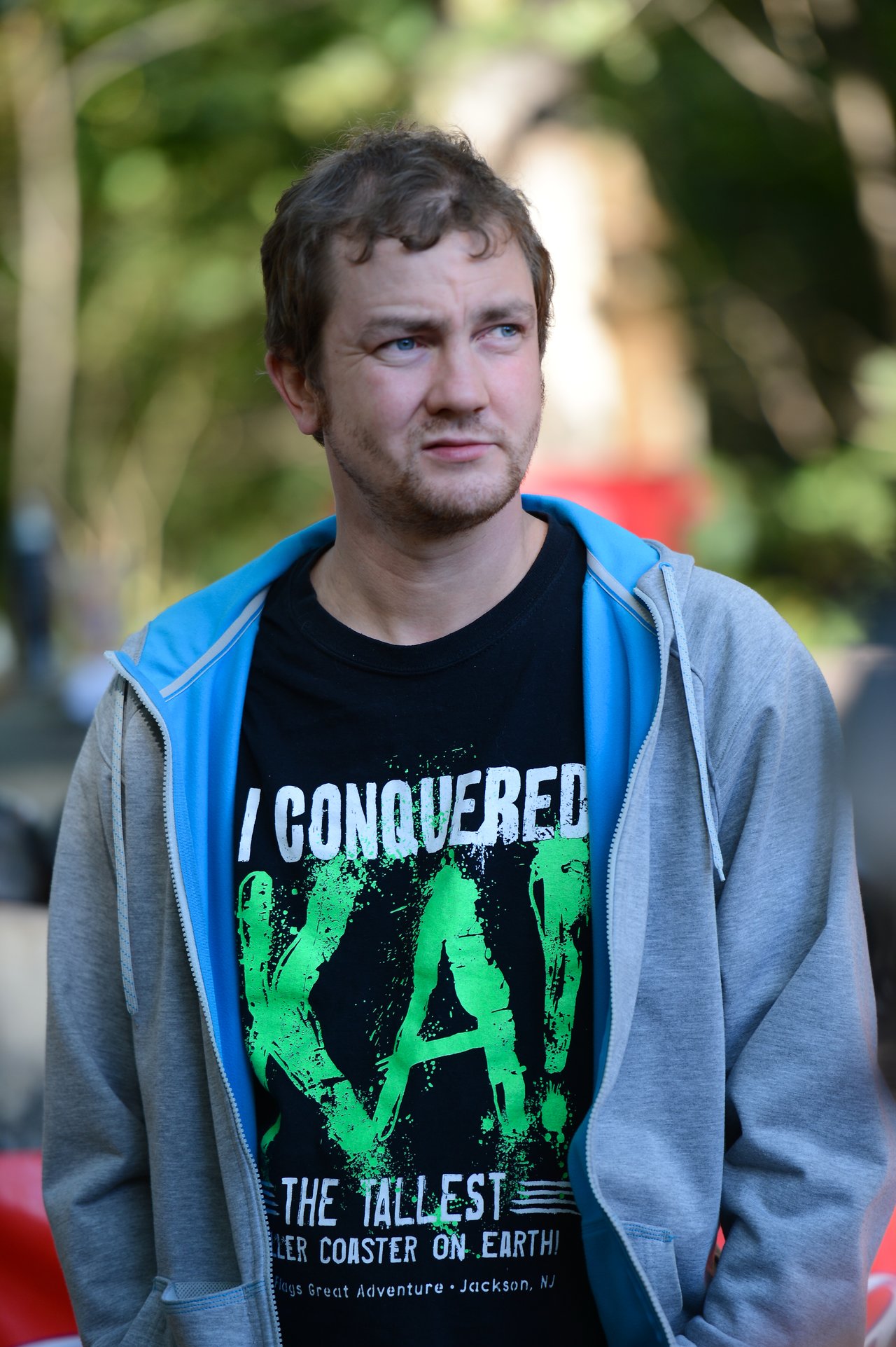 A man wearing a black T-shirt with bold green text stands outdoors, looking to the side.