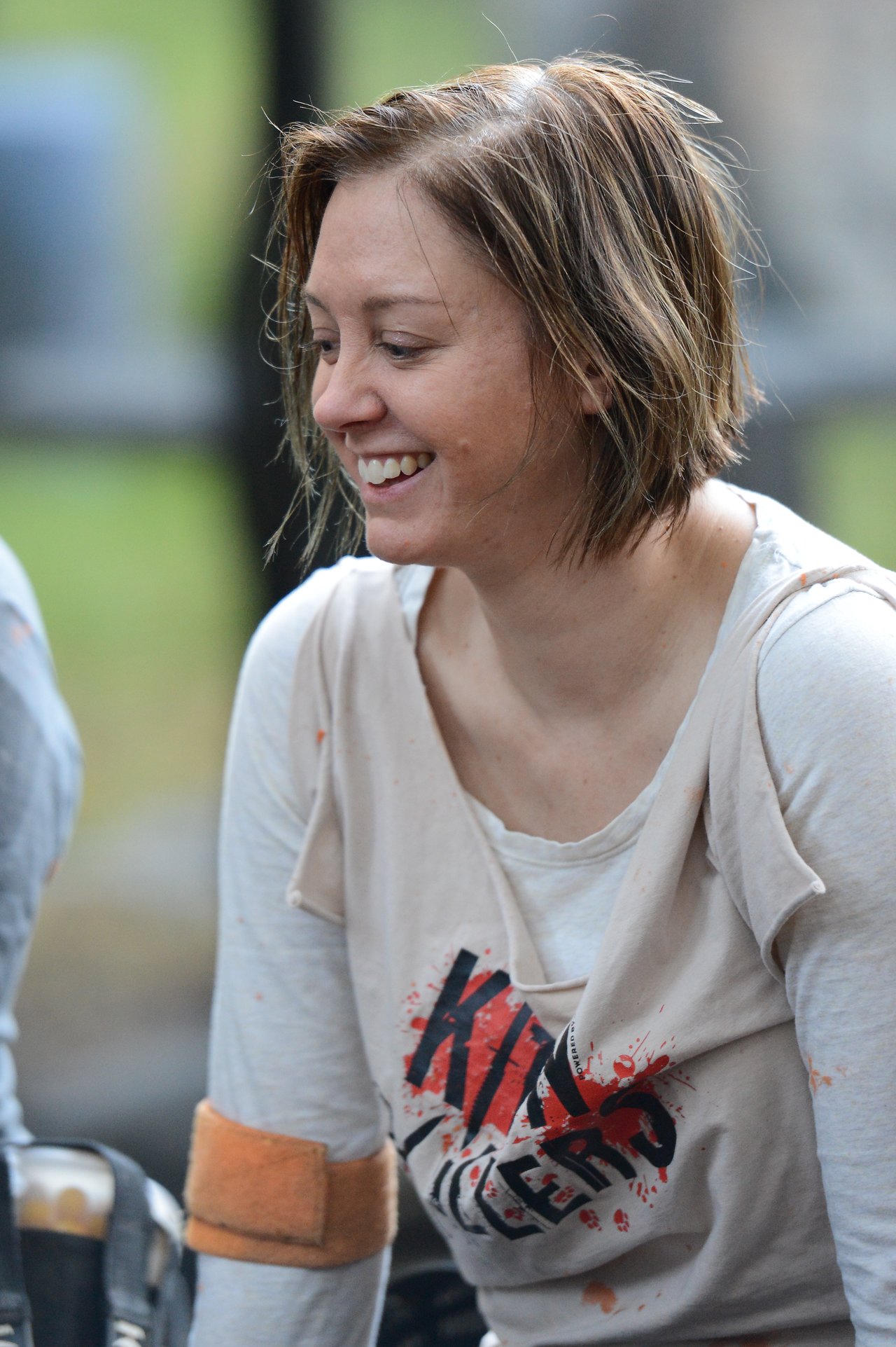 A smiling person wearing a distressed shirt with red text and an armband, engaged in an outdoor activity.