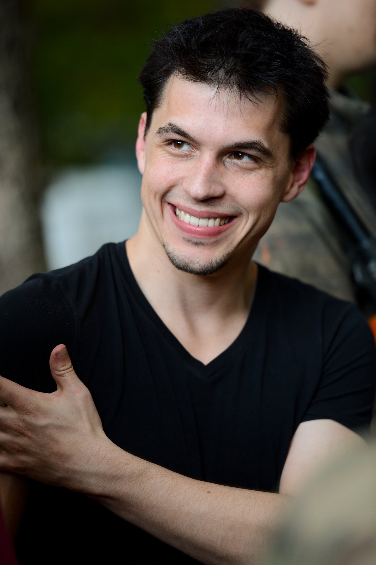 A person in a black shirt smiles while looking to the side, with one hand on their shoulder.
