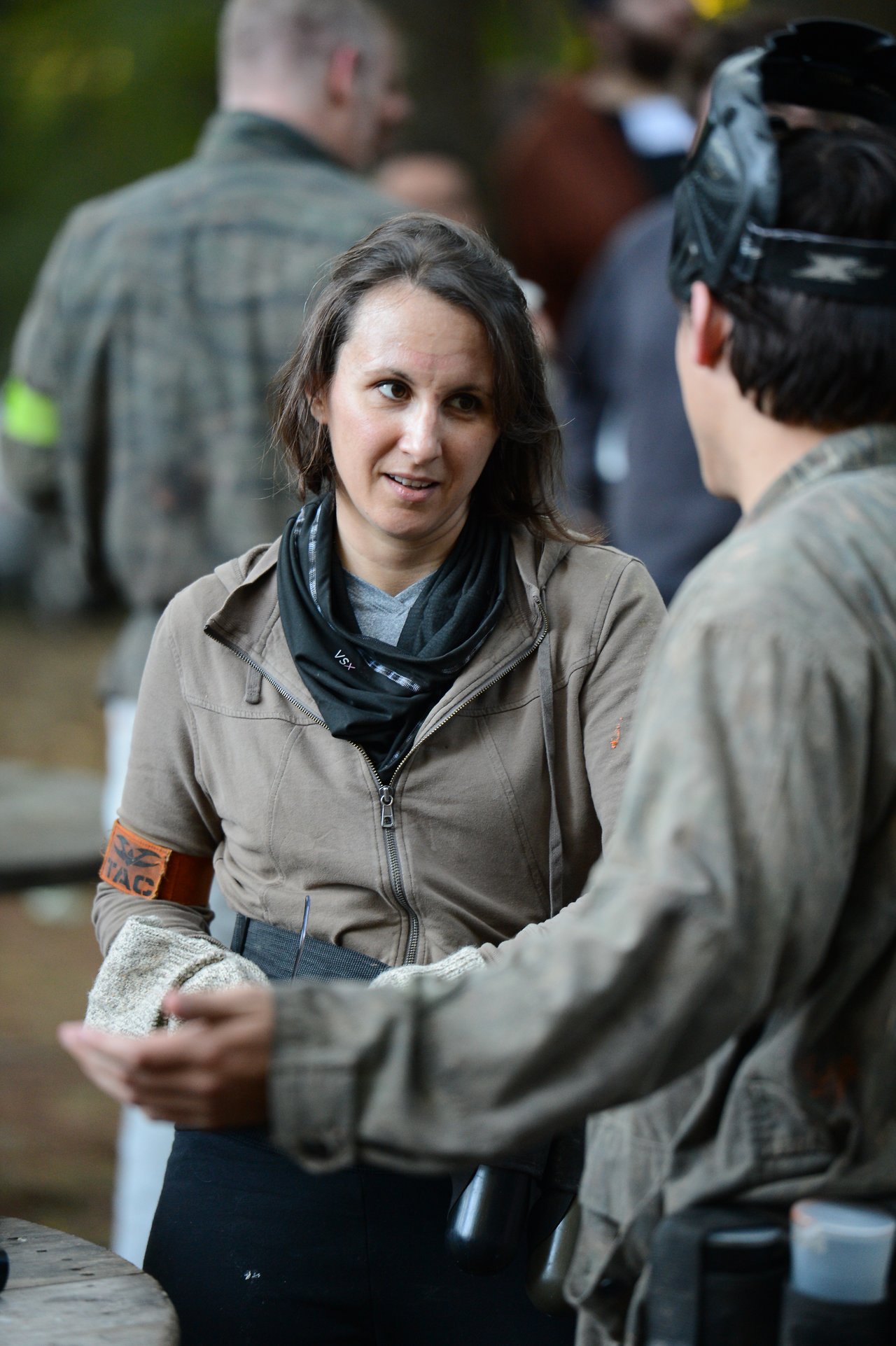 Two people in paintball gear are having a conversation, with one gesturing while the other listens attentively.