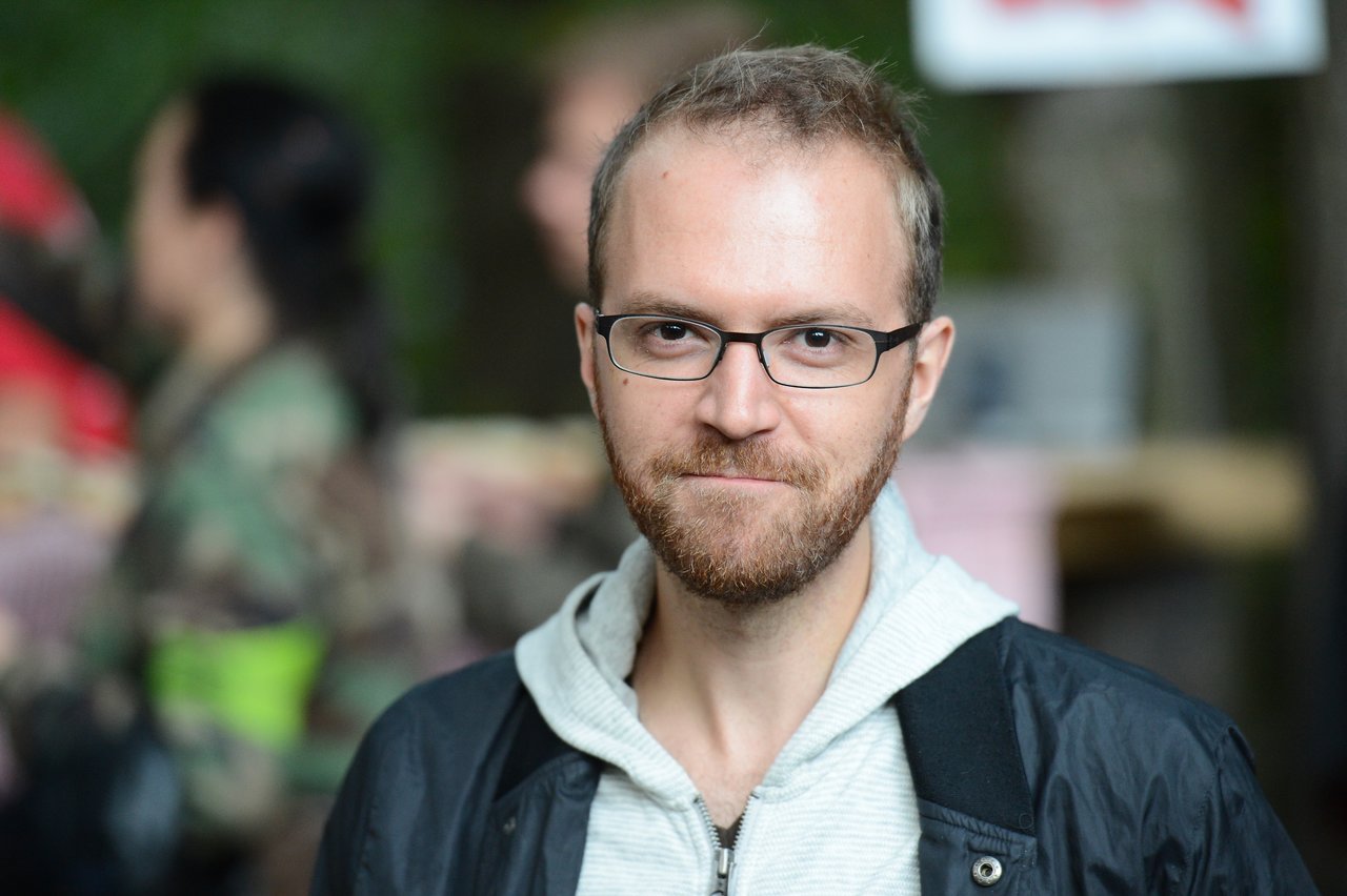A man with glasses and a beard looks at the camera with a slight smile at an outdoor event.