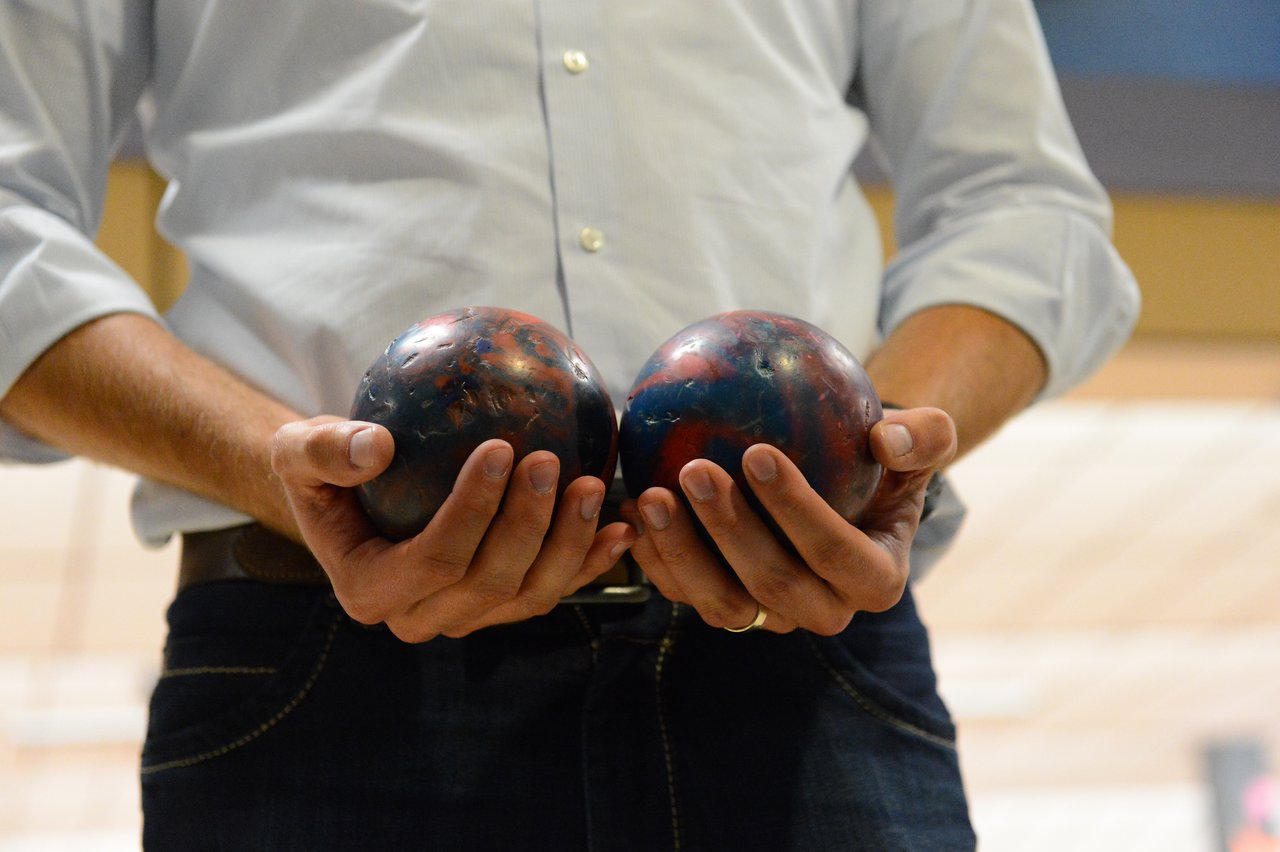 A person in a light-colored shirt holds two small bowling balls, one in each hand.