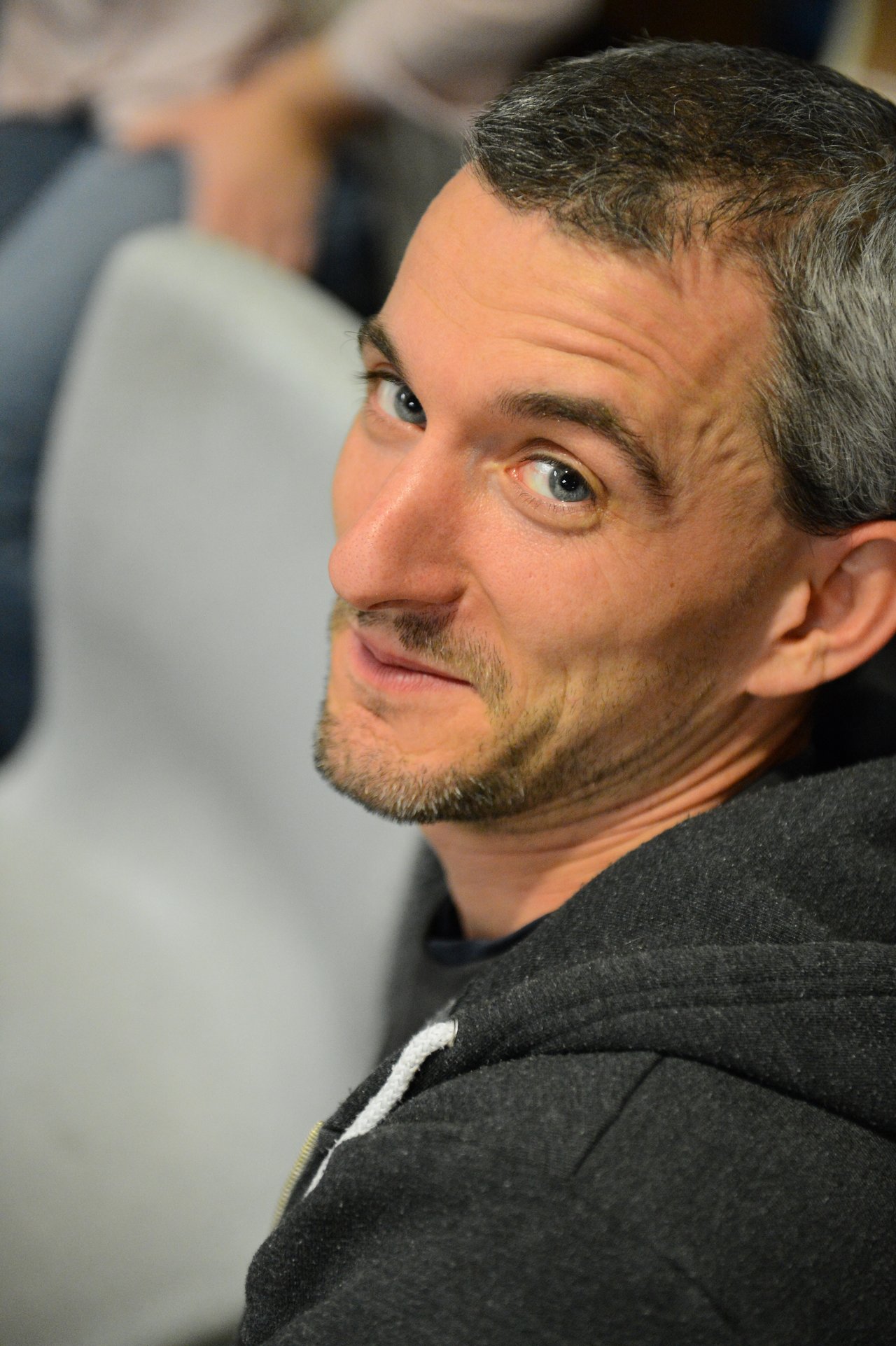 A man in a dark hoodie looks back at the camera with a slight smile.