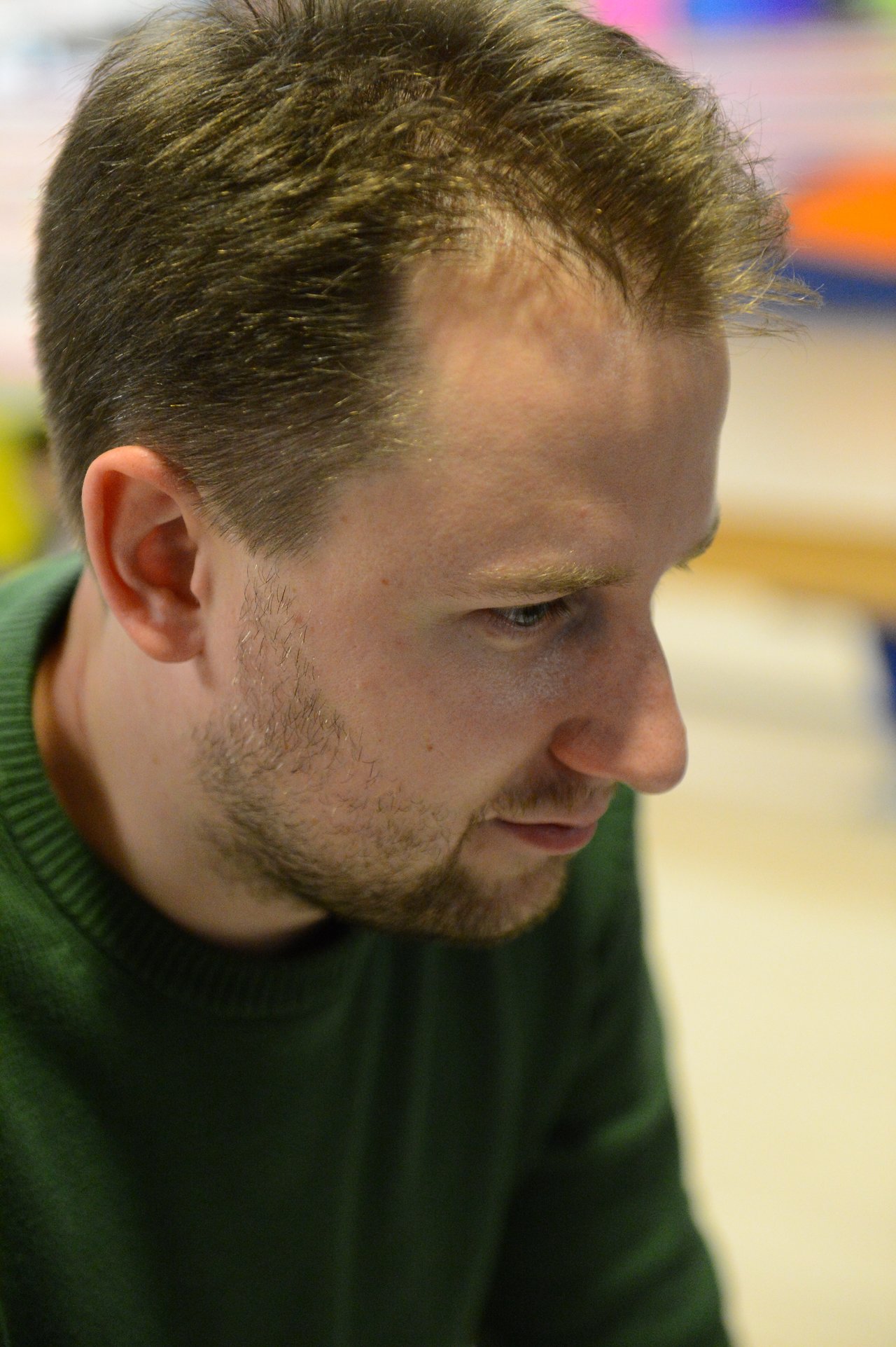 A man in a green sweater looks intently at something in front of him.